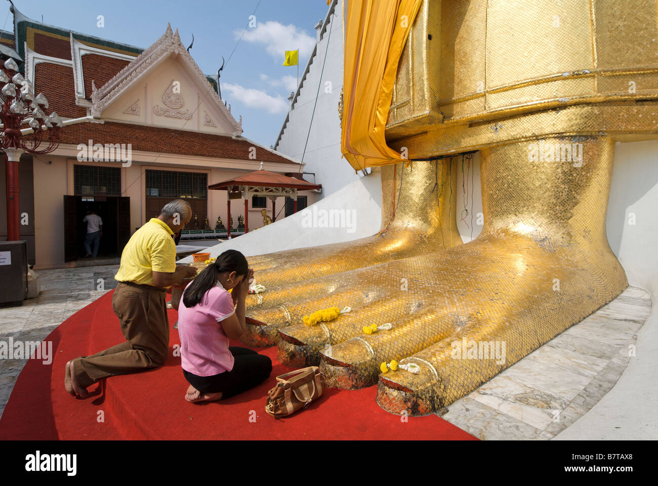 Buddhists praying at feet of 32m golden standing buddha Wat Intharavihan temple in Dusit district of Bangkok in Thailand Stock Photo