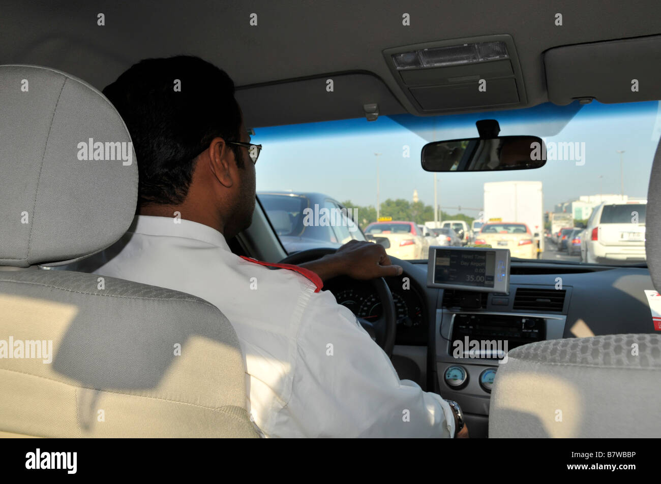 Interior close up back view Dubai taxi cab worker driver hand on steering wheel driving along busy road stuck in traffic jam United Arab Emirates UAE Stock Photo