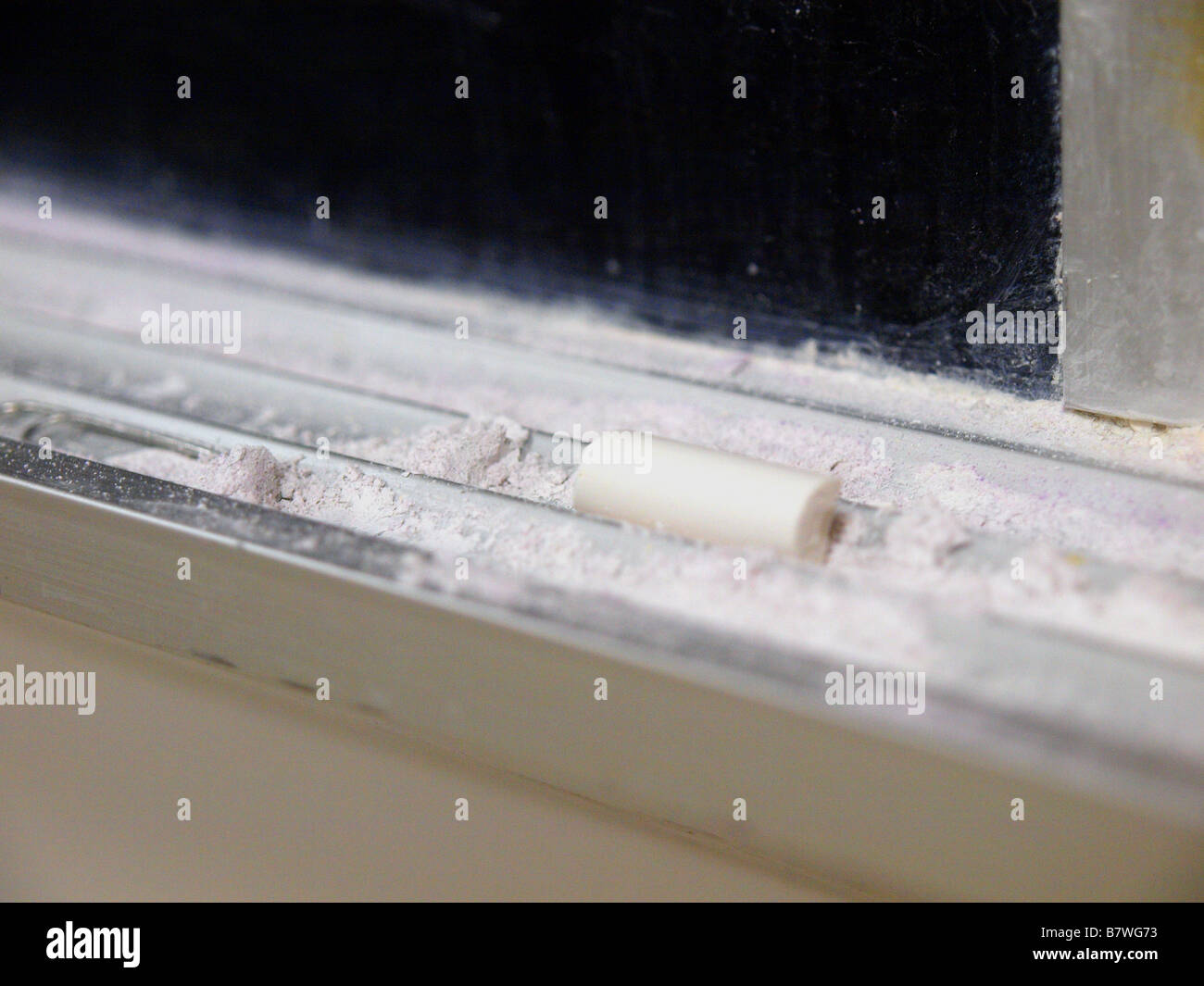 A stick of chalk on a messy chalk tray beneath a blackboard in an aging