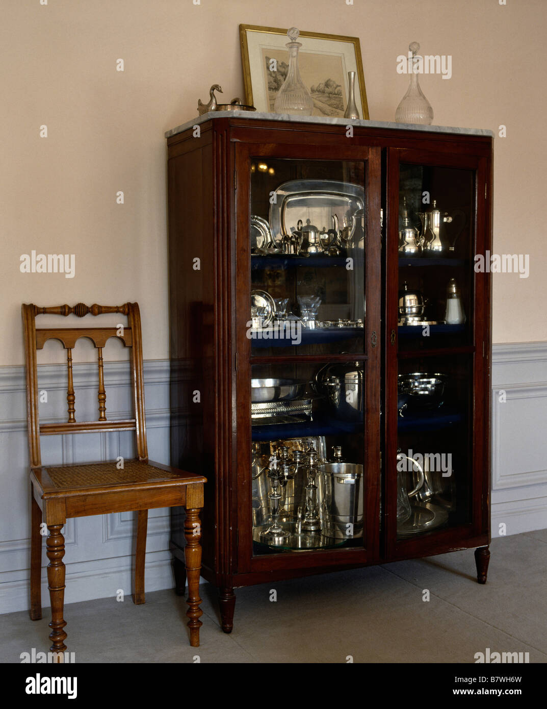 Antique dining chair beside glass-fronted cupboard with collection of  silverware and chrome coffee pots Stock Photo - Alamy