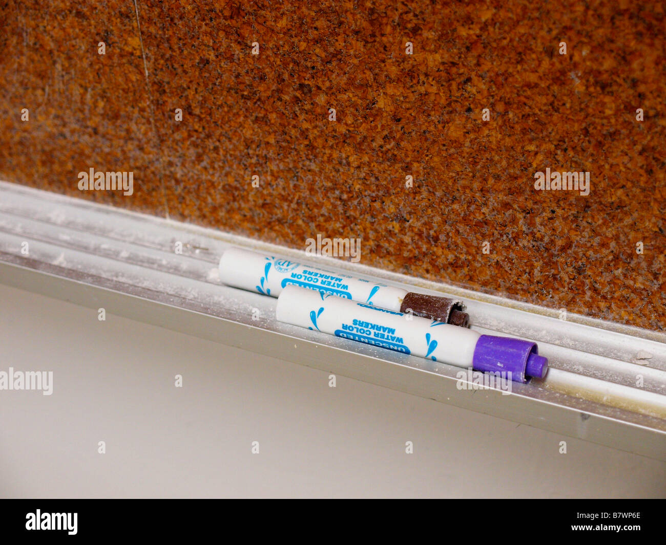 Two dryerase markers on a tray below a corkboard in a college