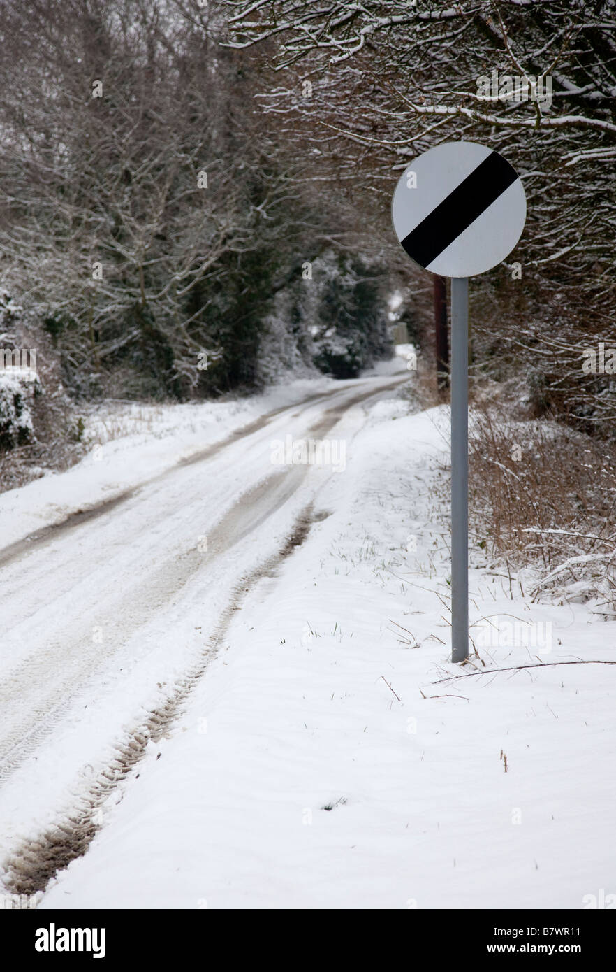 UK national speed limit (60 mph or 70 mph) sign on a snow covered road with overhanging trees. Stock Photo