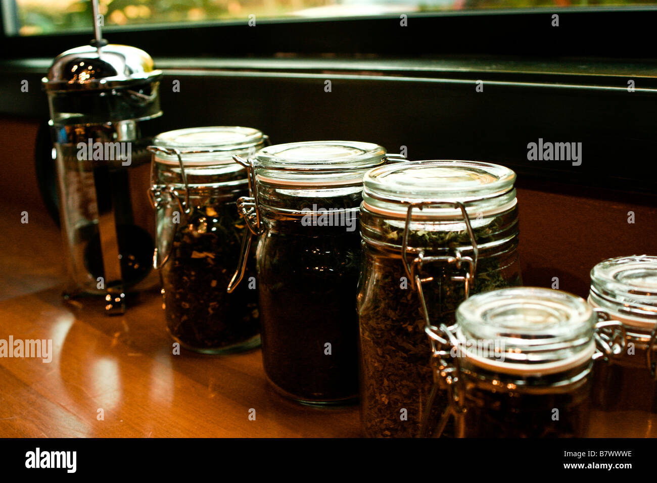 A french press and glass jars filled with tea lined up on a window sill