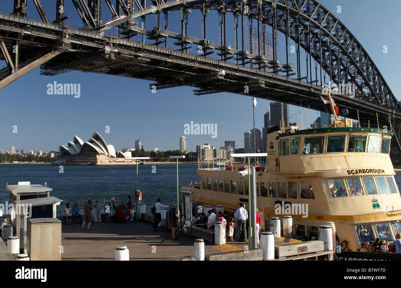 Milsons Point ferry stop with a ferry in the foreground and Sydney harbour bridge and the Sydney Opera House in the background Stock Photo