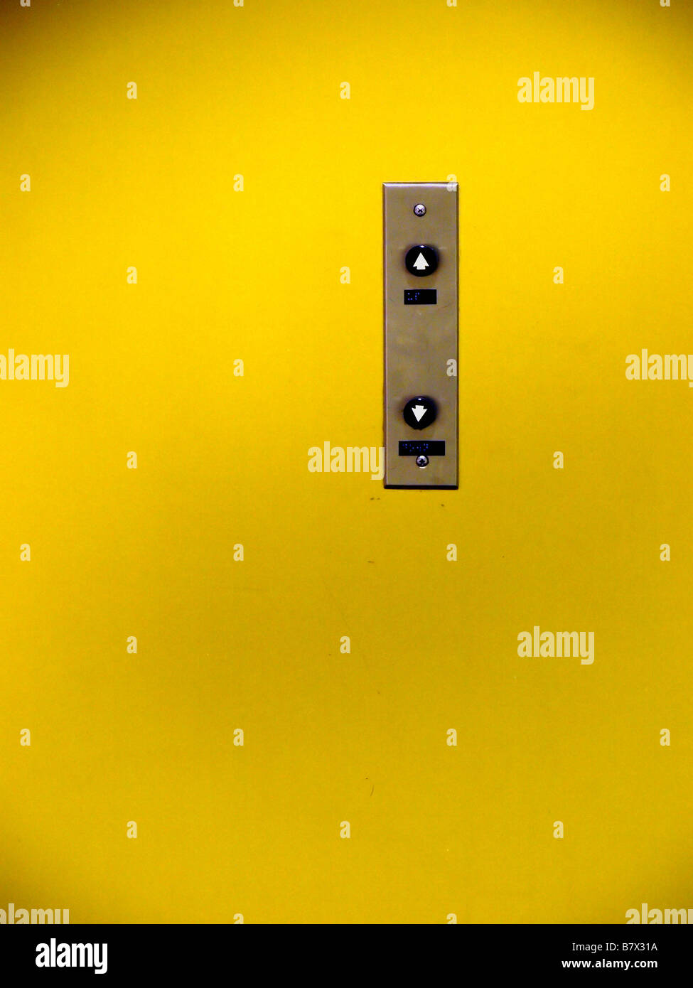 Vintage up and down elevator buttons on a stainless steel panel in the middle of a painted yellow wall. Stock Photo