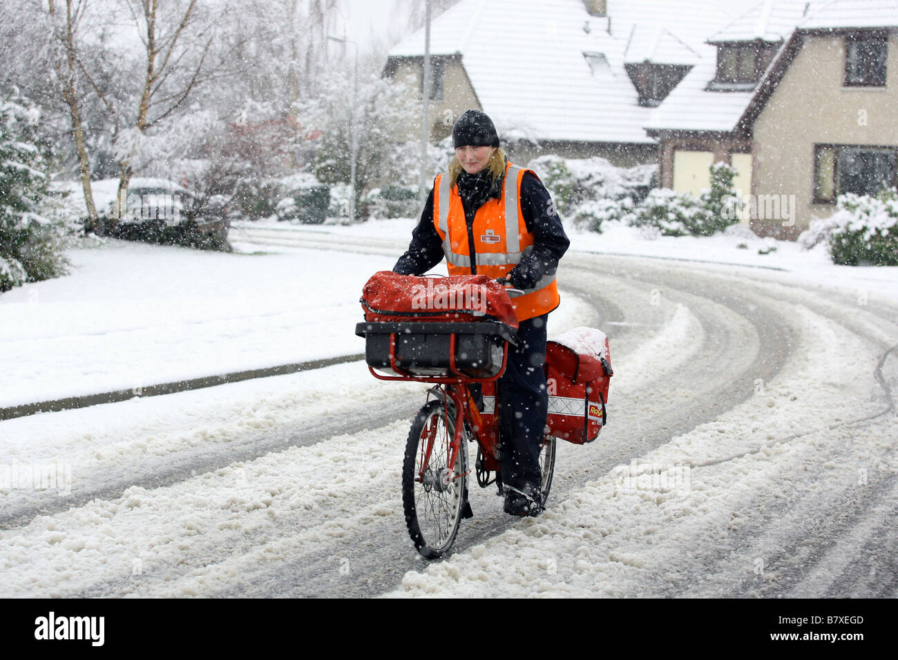 Woman postal worker cycling in snowy roads in Aberdeenshire, Scotland, UK, during winter Stock Photo