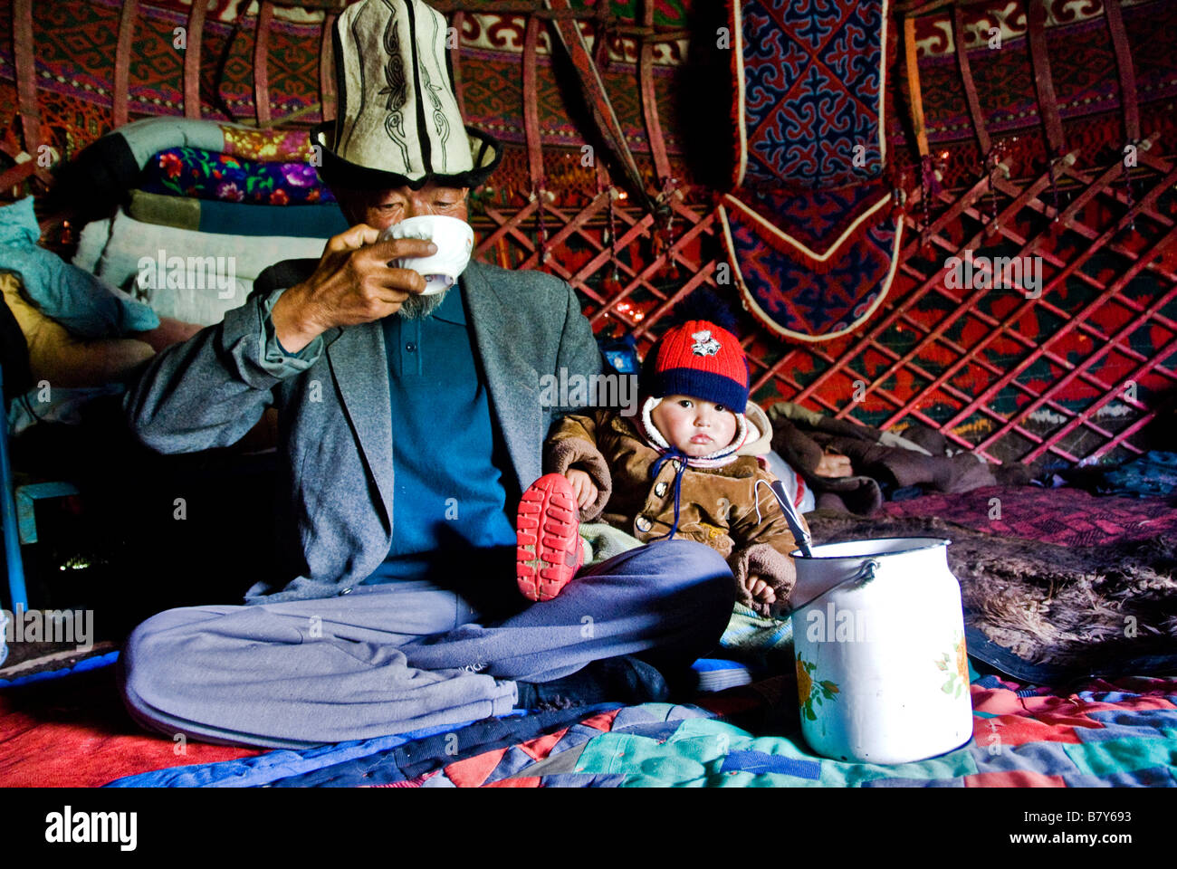 Old Kyrgyz man and grandson drinking horse milk inside his yurt Kyrgyzstan Stock Photo