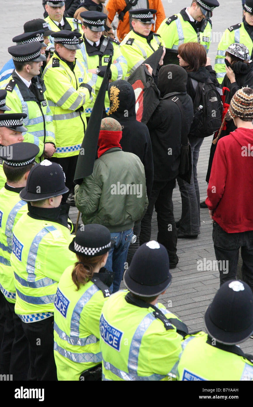 Young protesters confront police on London's South Bank. They are waving an Anarchy banner. Stock Photo