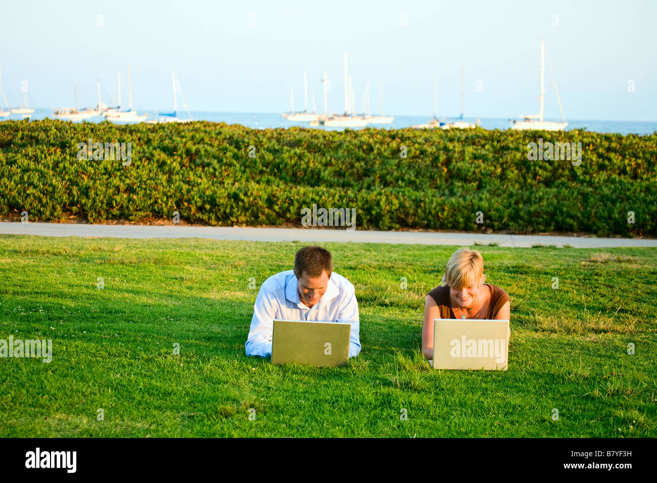 A modern couple is distance learning outside in a park on their laptop computers. Stock Photo