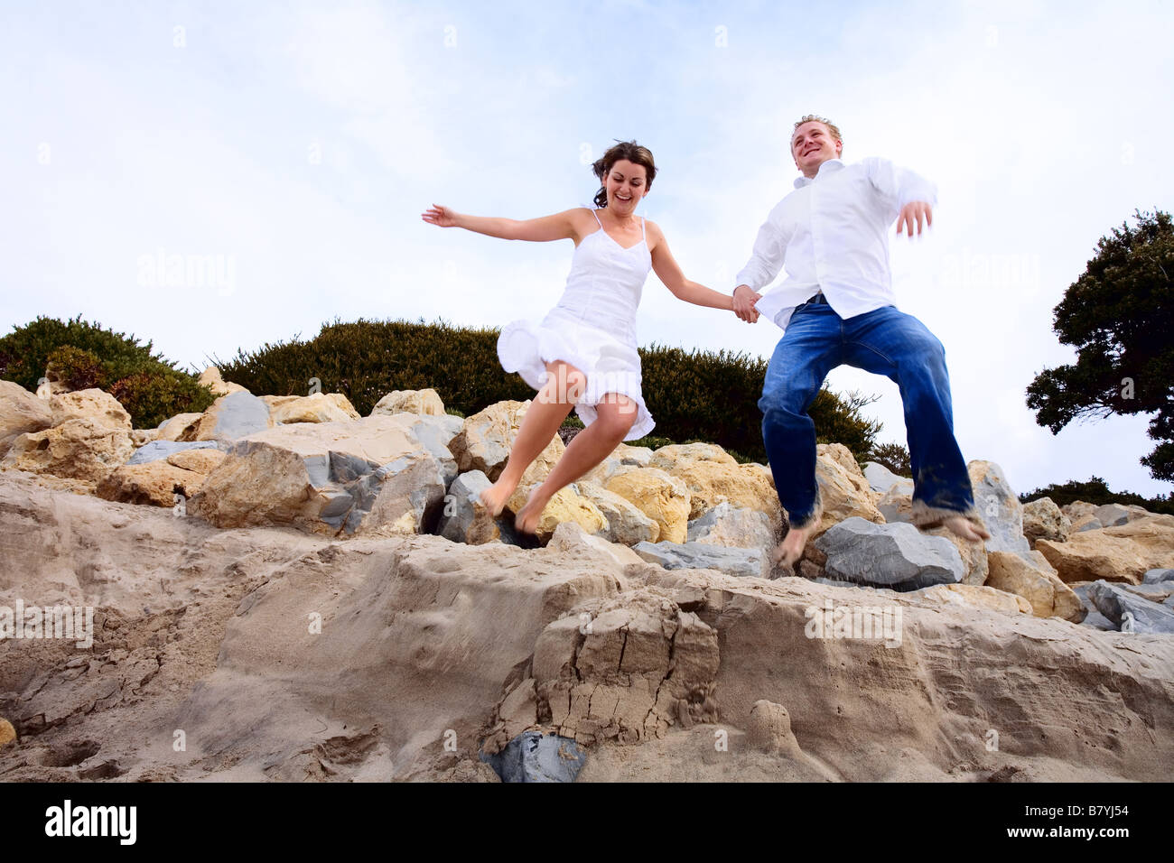 A romantic couple jumping at the of the rocks at the beach Stock Photo ...