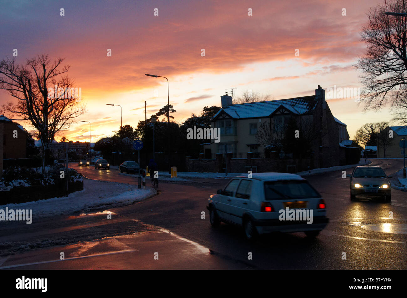 Sunset and reflections winter roundabout road scene with snow on paths Downend Bristol Stock Photo