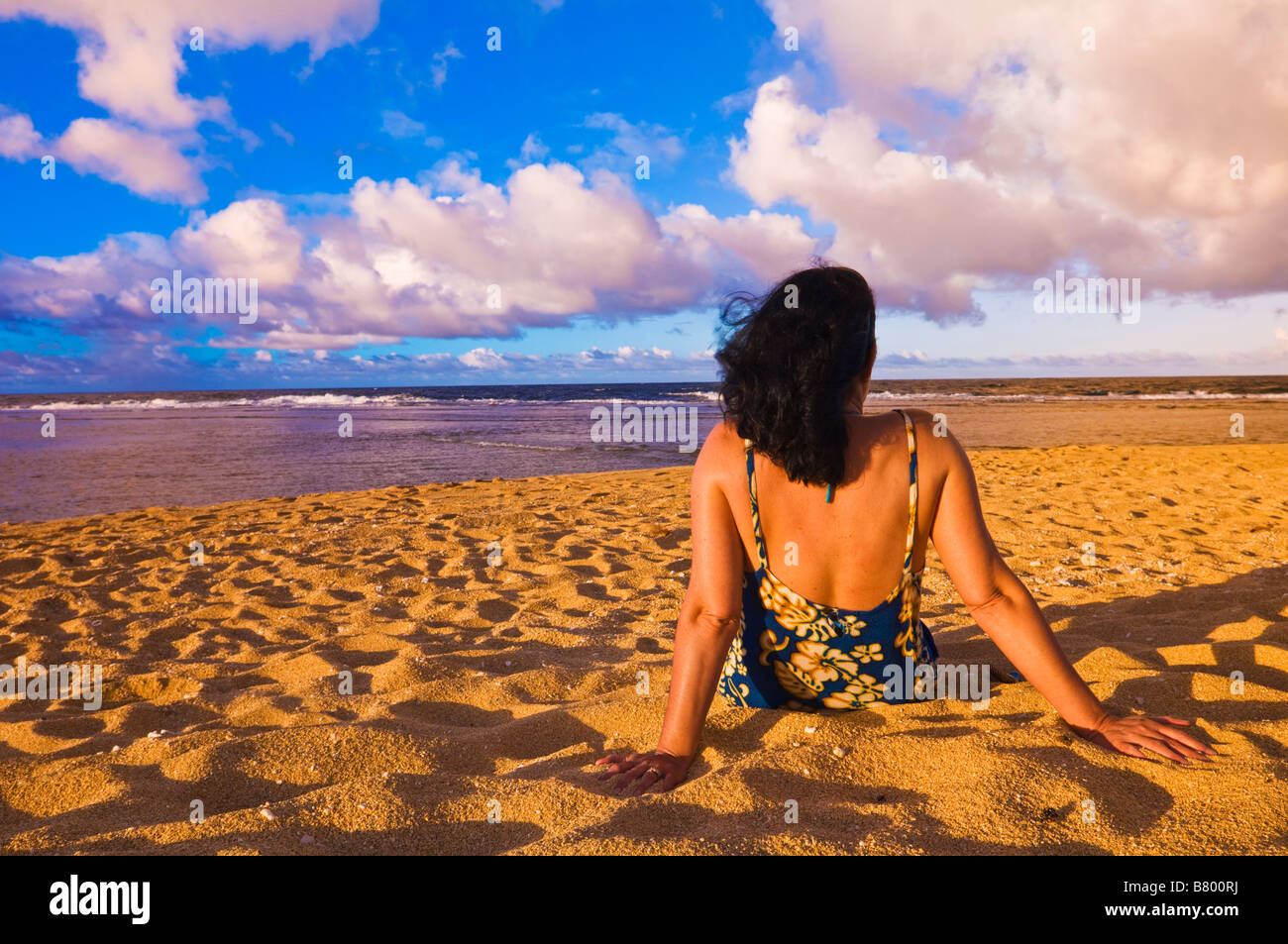 Woman sitting on Tunnels Beach at sunset North Shore Island of Kauai