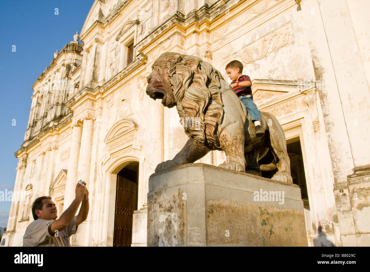 Leon Cathedral, Spanish colonial architecture, with Nicaraguan man photographing boy on lion statue flanking entrance Stock Photo
