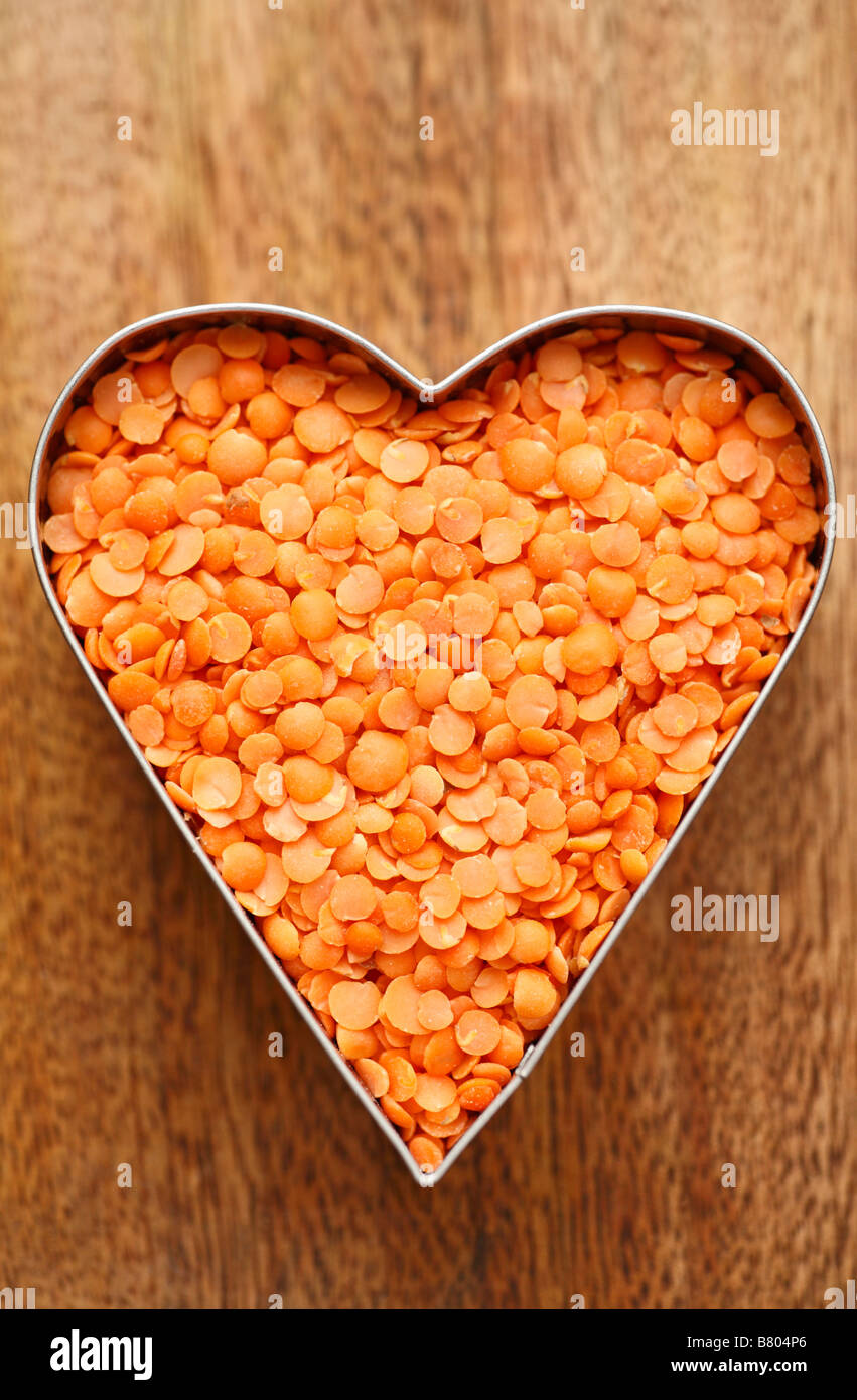 Red lentils held inside a heart shape. Stock Photo