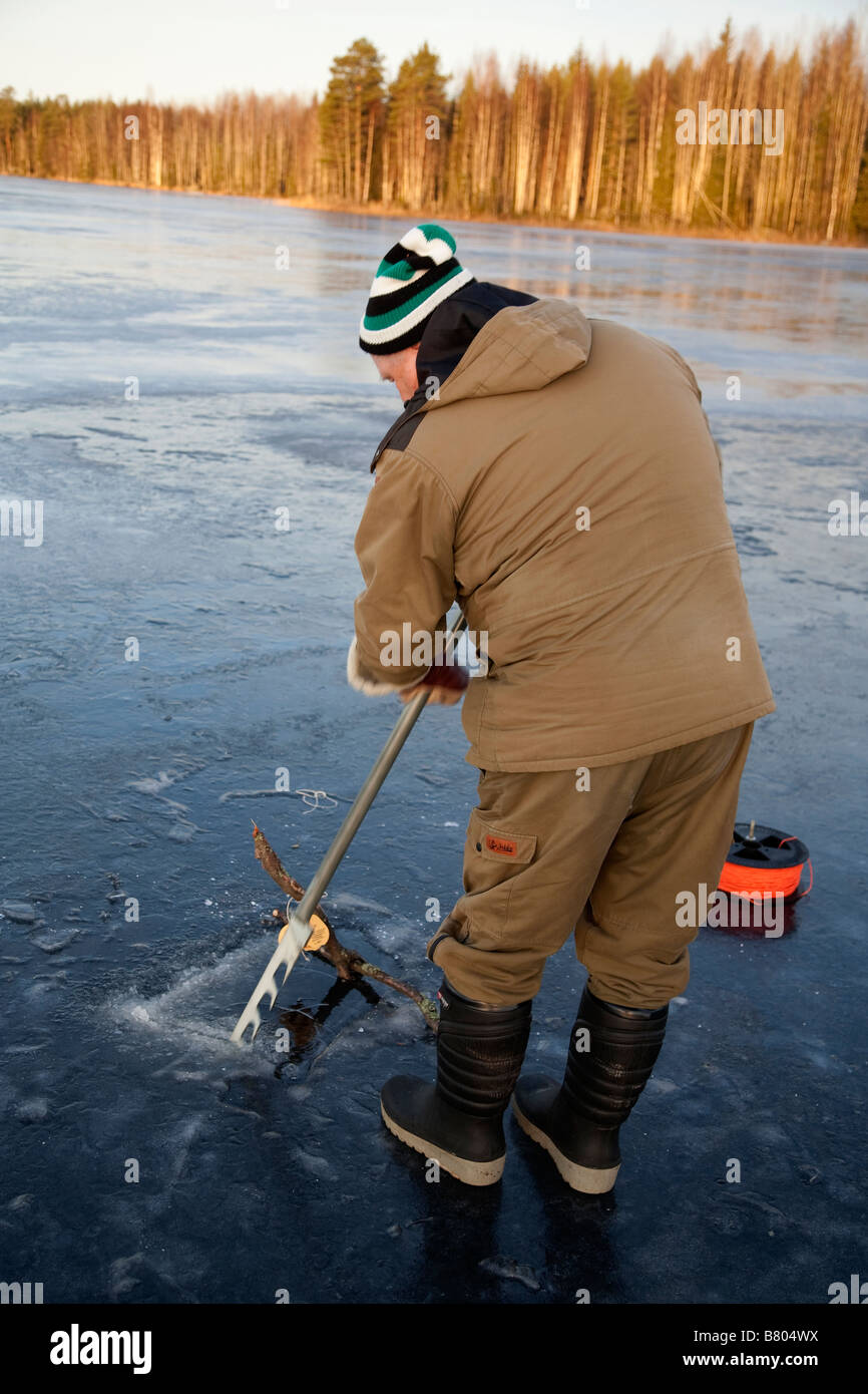 Elderly man sawing a hole in the ice for fishing nets, using an