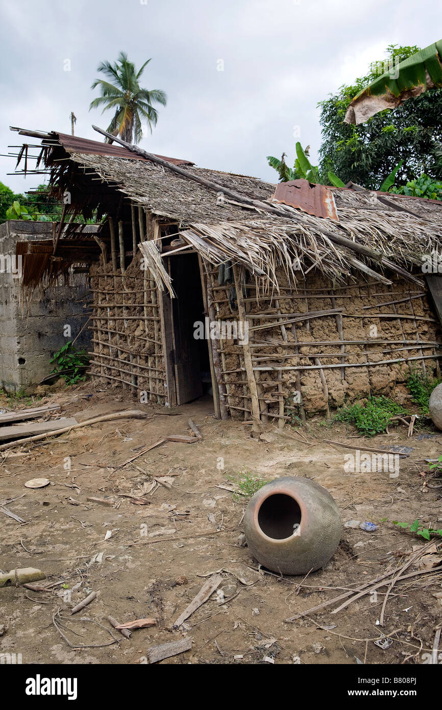 An old clay pot sits on the ground in front of an incomplete wattle and daub house in a remote stormy jungle village of Nigeria Stock Photo