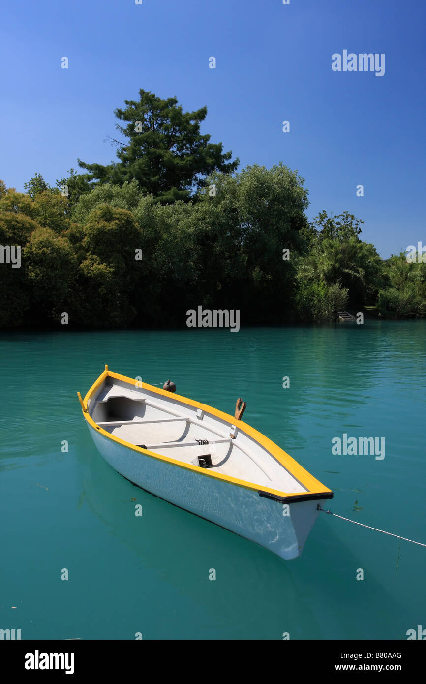 A clean white boat floating on a deep green river trees and blue sky in background Stock Photo