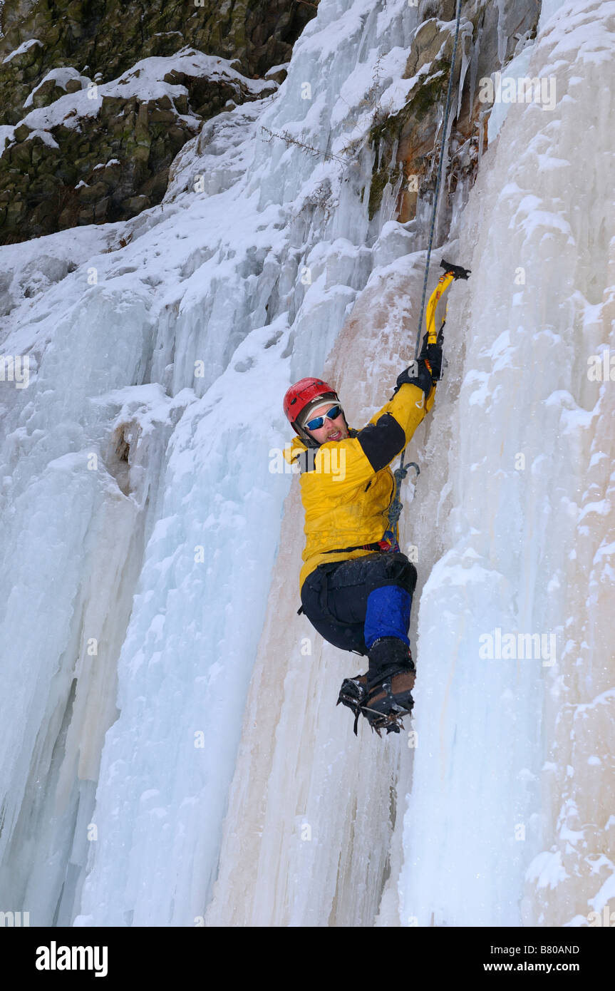 Ice climber on belay hanging on and looking for foothold on a wall of ...