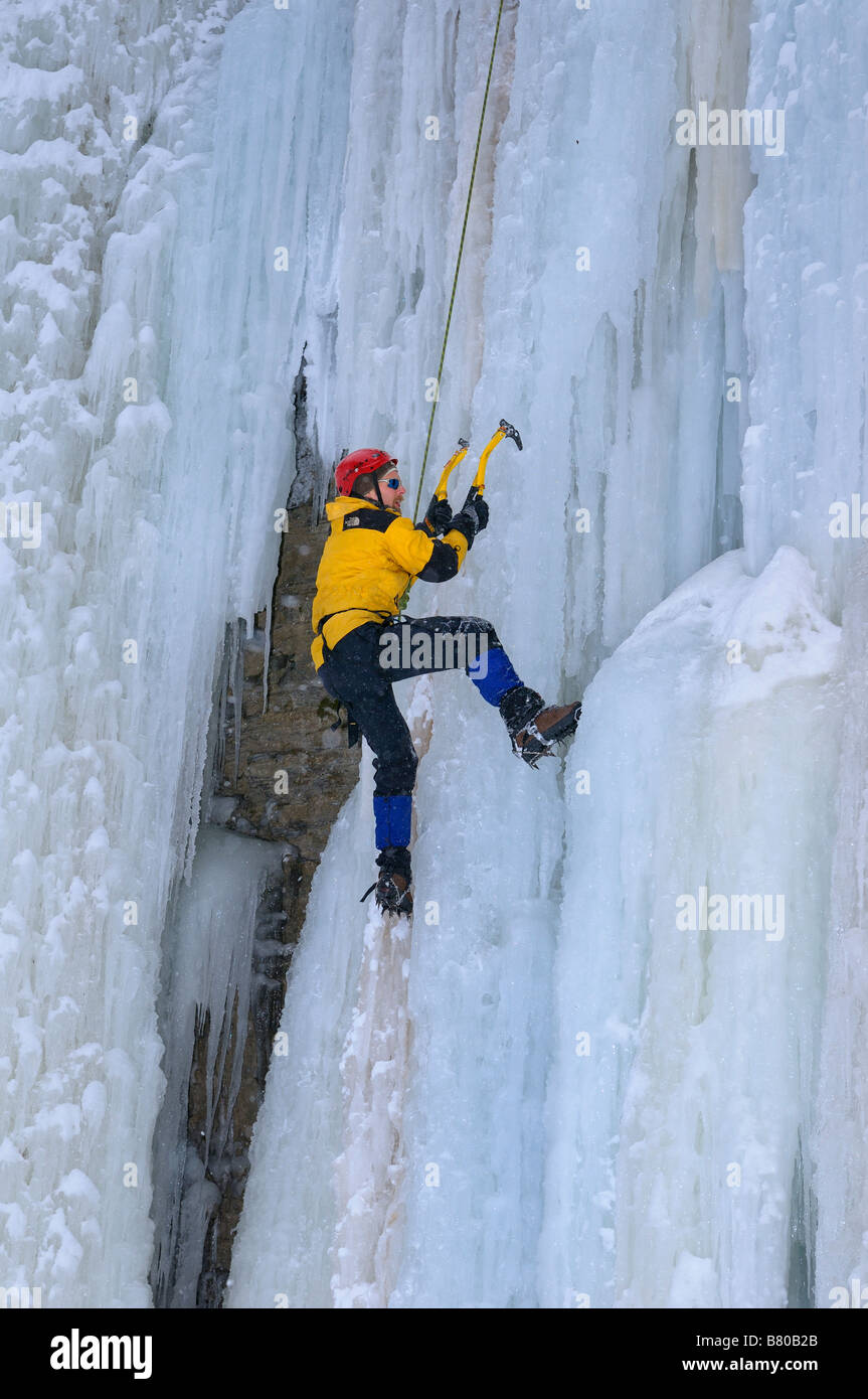 Ice climber front pointing up a steep icefall with top rope belay at