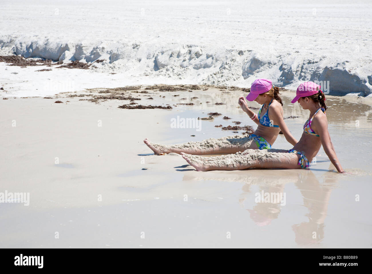 Two young teenaged girls cover their legs with sand on Gulf of Mexico beach at St Joseph Peninsula State Park in Florida Stock Photo