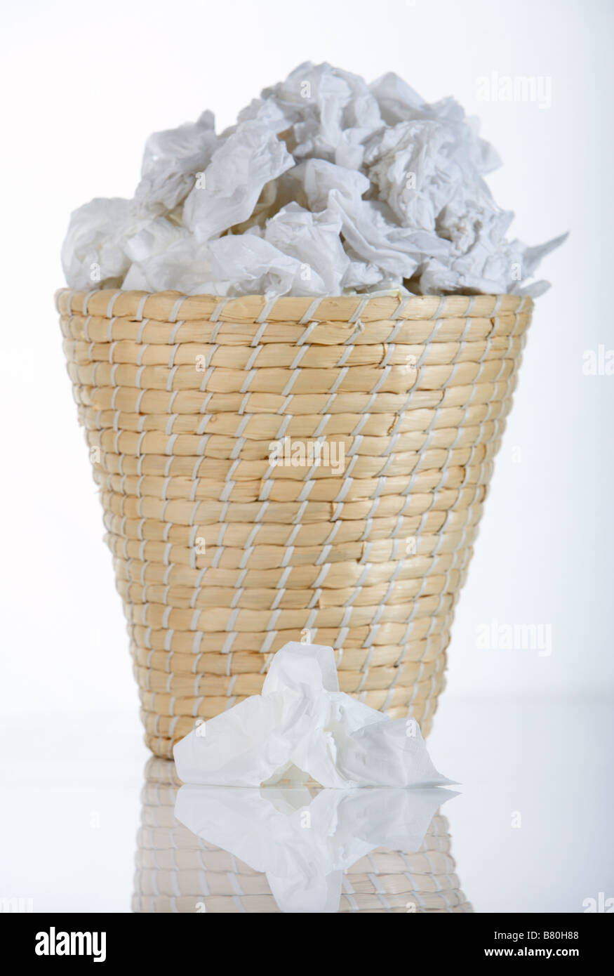 wicker waste paper basket bin full of used tissues with single used tissue lying in front of bin Stock Photo