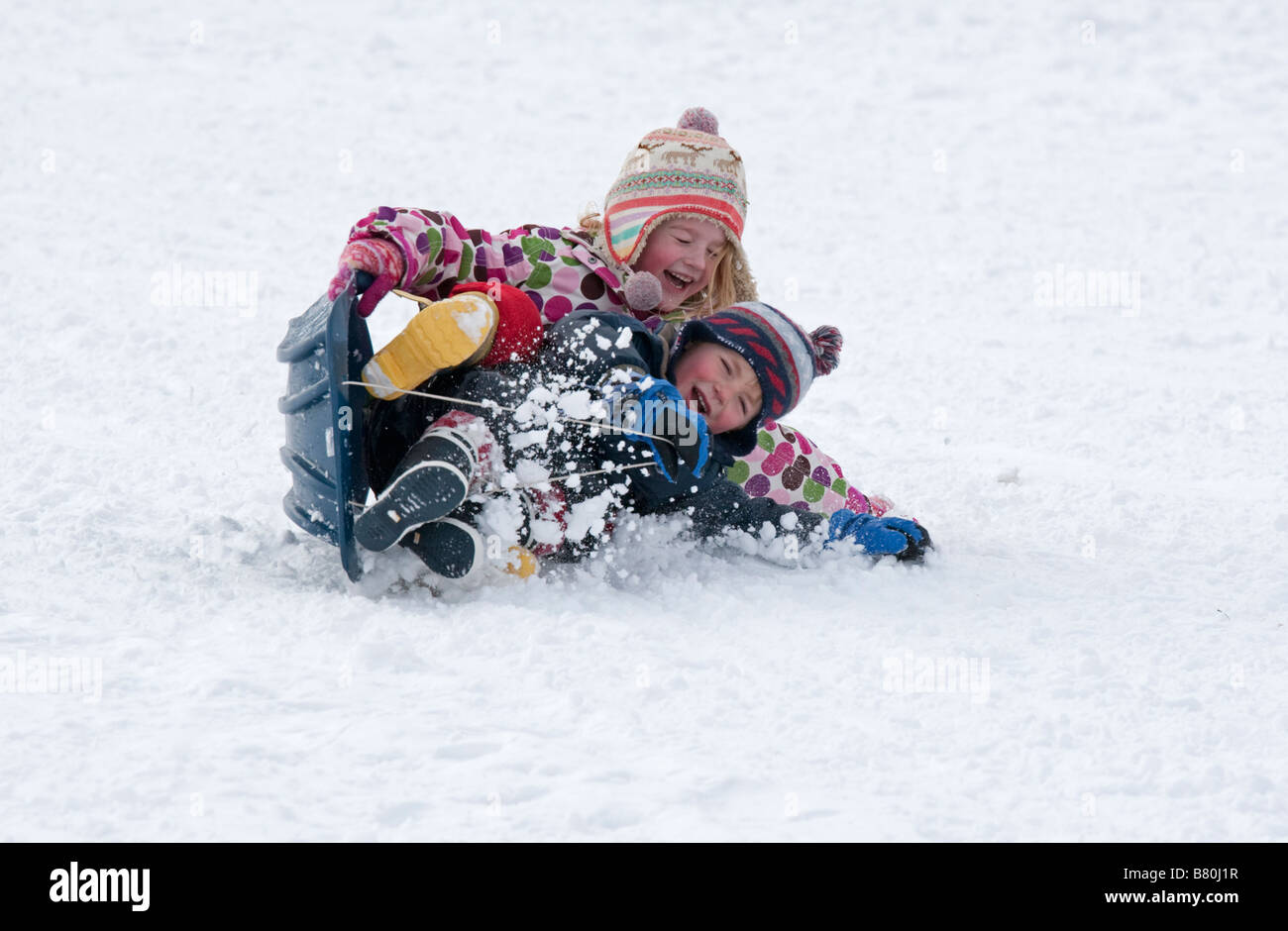 Young children falling off sledge in deep snow Cleeve Hill Cotswolds UK