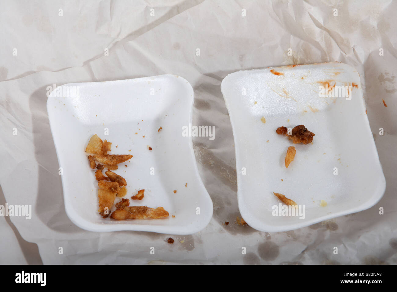 two used polysterene chip cartons fast food with remnants of chips and sauce on greasy white paper Stock Photo