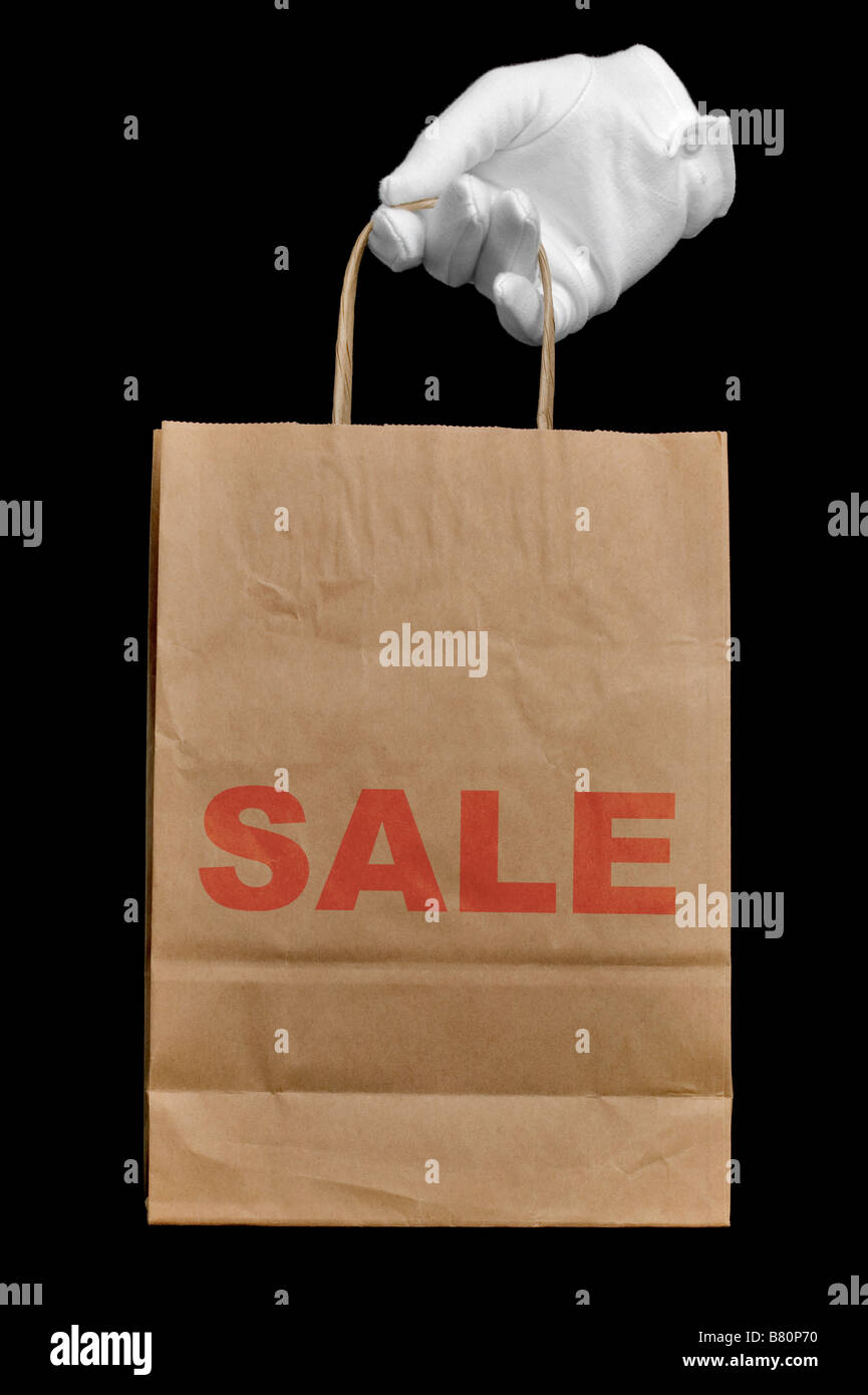 Hand in a white glove holding a brown recycled paper shopping bag with the word SALE written on it isolated on black Stock Photo