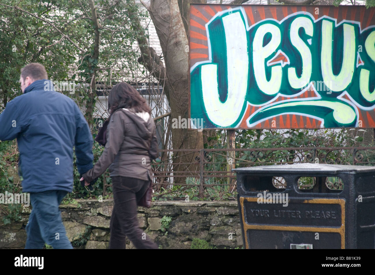 two people walk past a Jesus sign in Falmouth, UK Stock Photo
