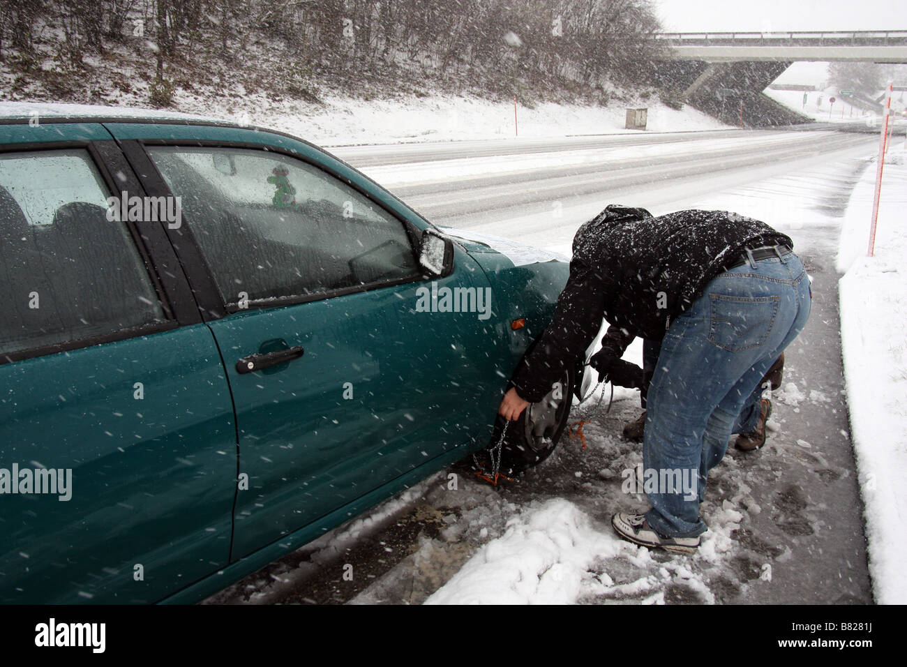 A man tries to attach tire chains to the front wheel of his car under a