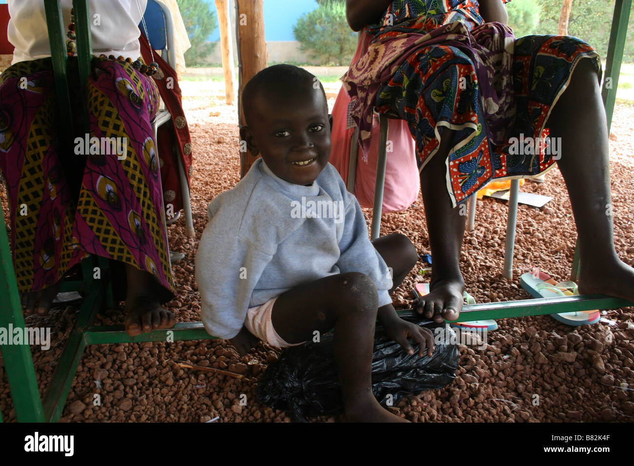 African child under the table of the women fabric bead makers in Burkina Faso. Charity for women against female circumcision Stock Photo