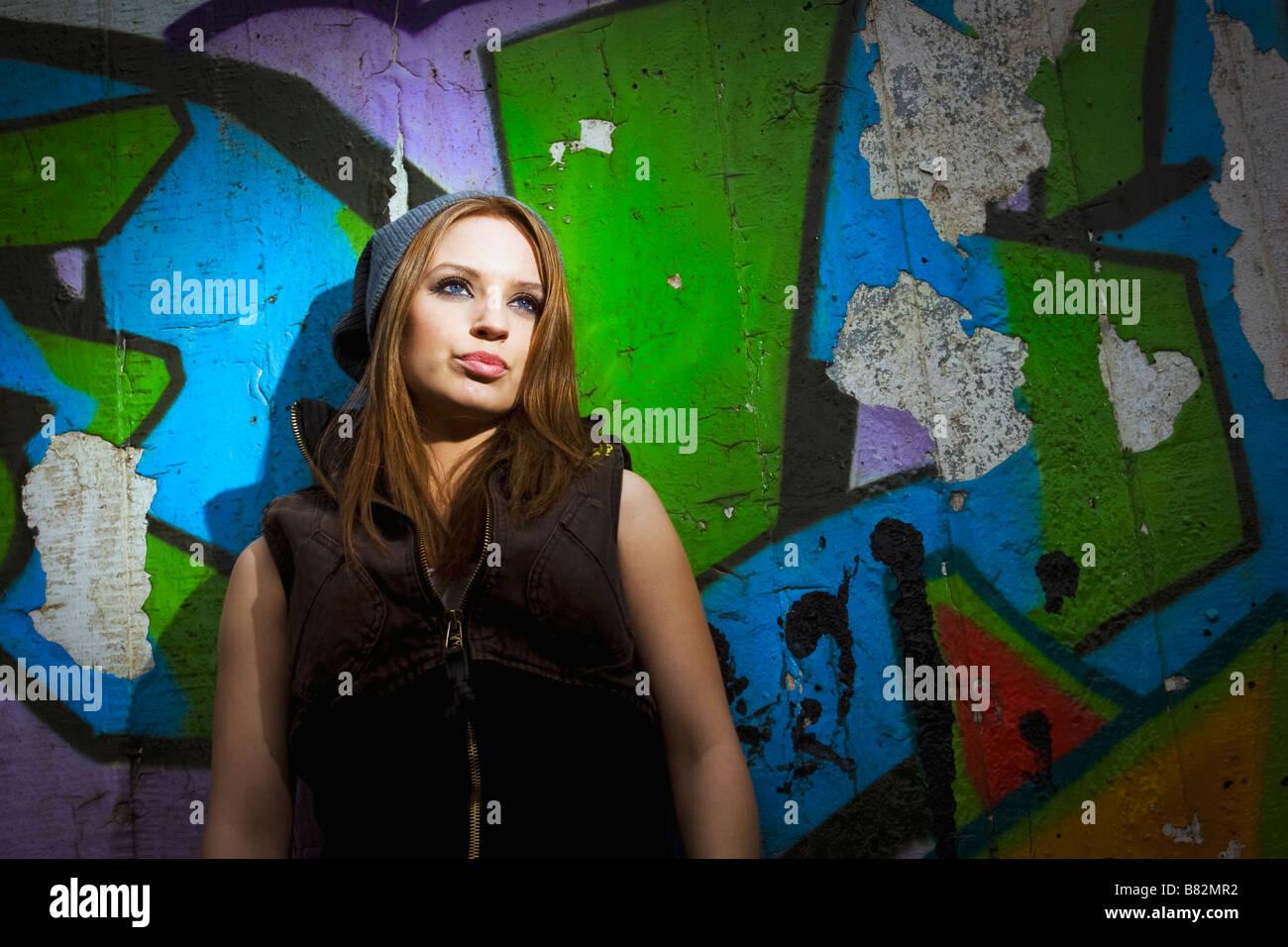 Young woman stands against graffiti in urban environment Stock Photo