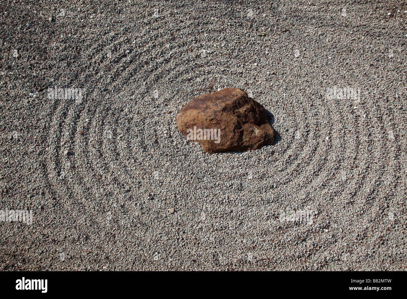 A tidy circular pattern rests around this anchoring rock in a Japanese rock garden  Stock Photo