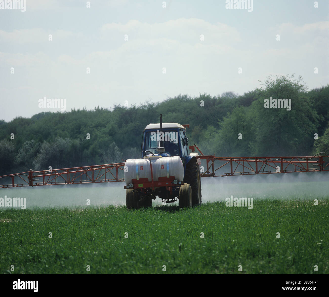 Ford tractor with 24 metre Lely boom sprayer and front mounted tank spraying young barley crop Stock Photo