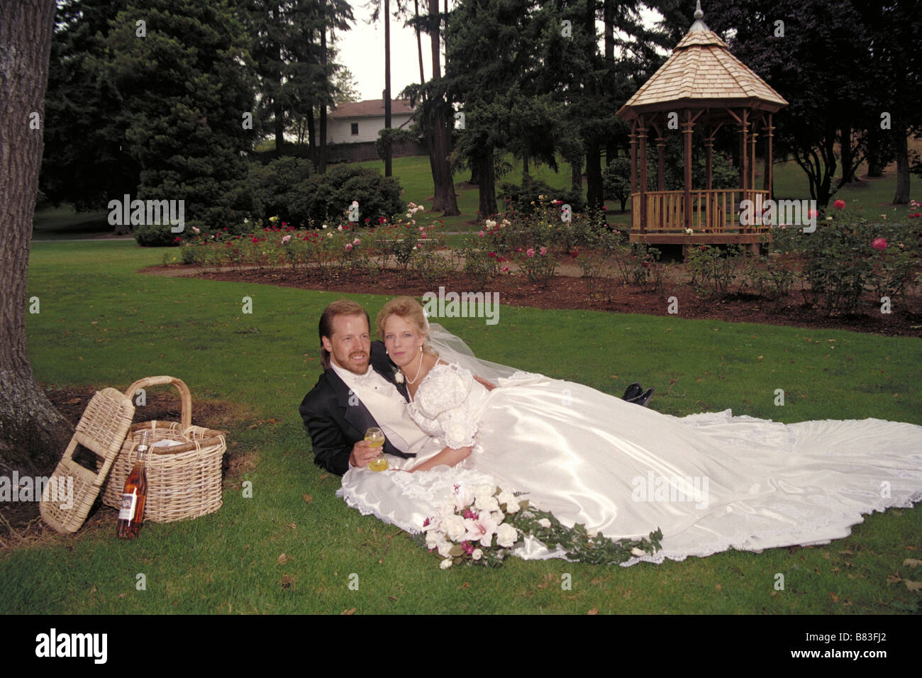 Bride and Groom lay in the grass and sip wine and picnic Stock Photo