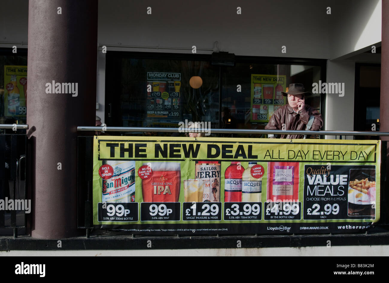 A man in Falmouth, UK on his phone outside a Wetherspoons pub advertising meal and drinks deals. Stock Photo