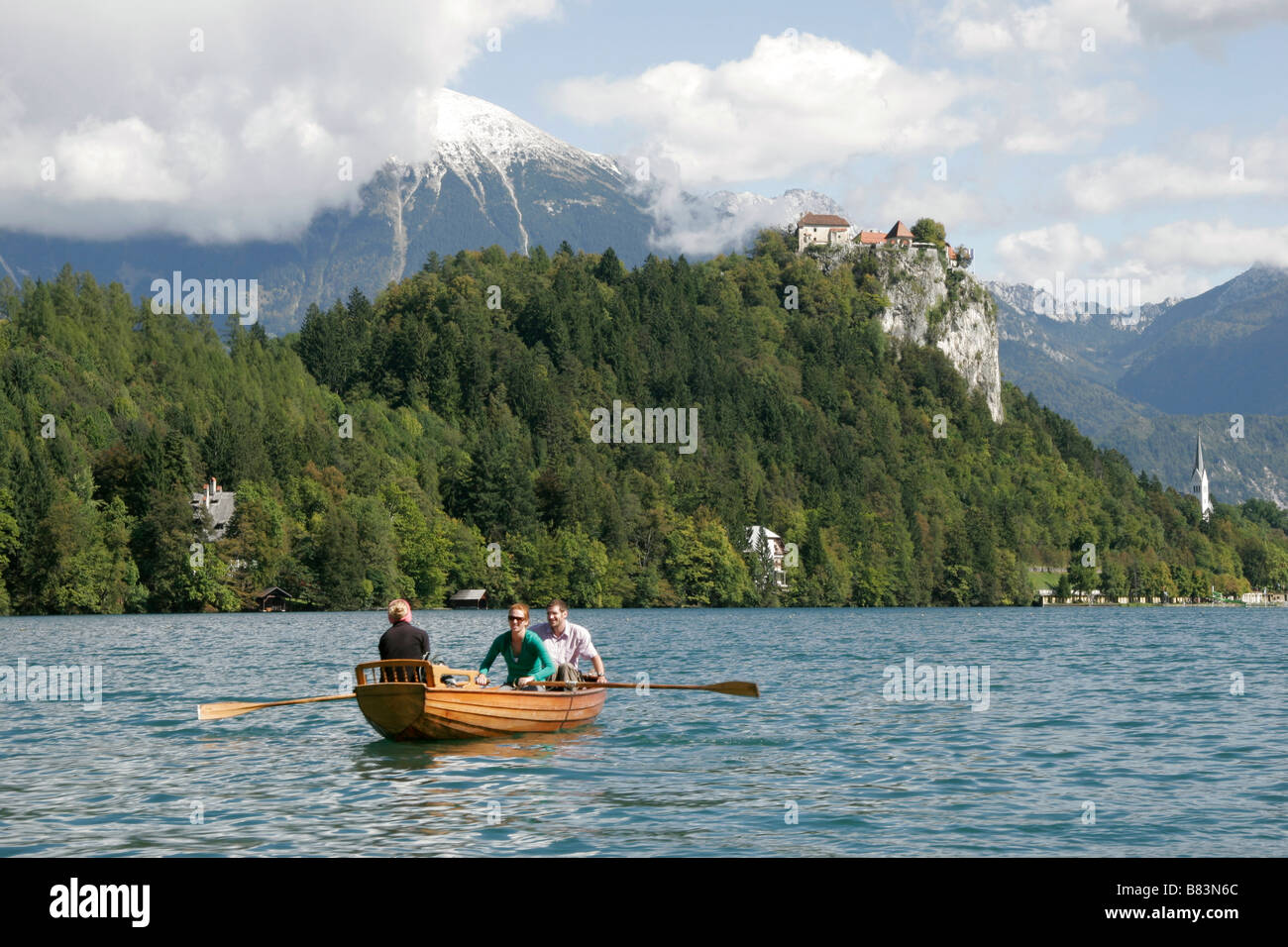 Tourists hire a rowing boat on Lake Bled, view of Bled Castle (Blejski Grad) and the Julian Alps