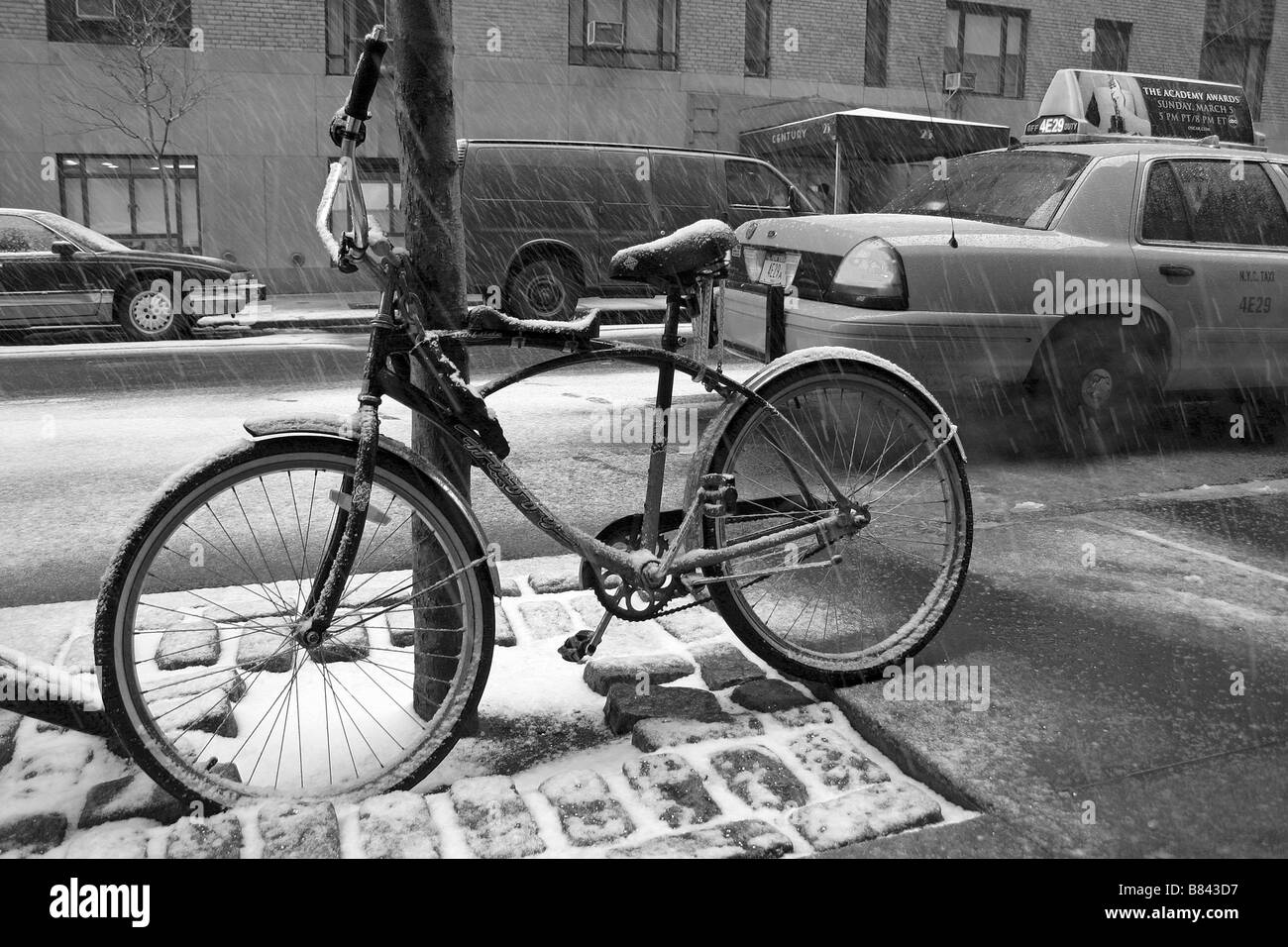 A bike stands in the snow as a taxi waits in the street, upper west side of Manhattan Island, New York City, USA Stock Photo