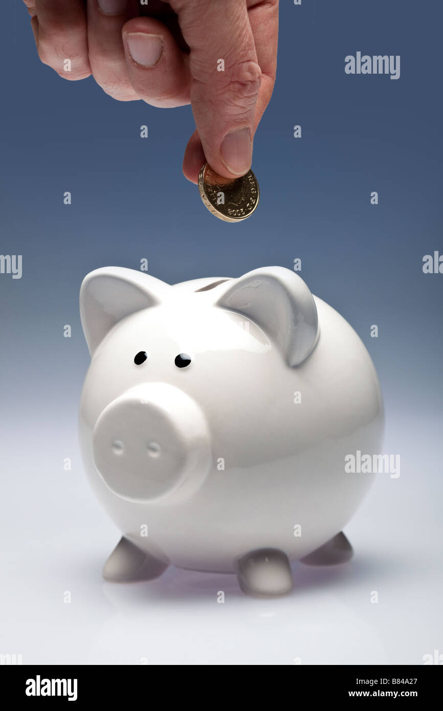 Piggy bank with fingers putting a coin in Stock Photo