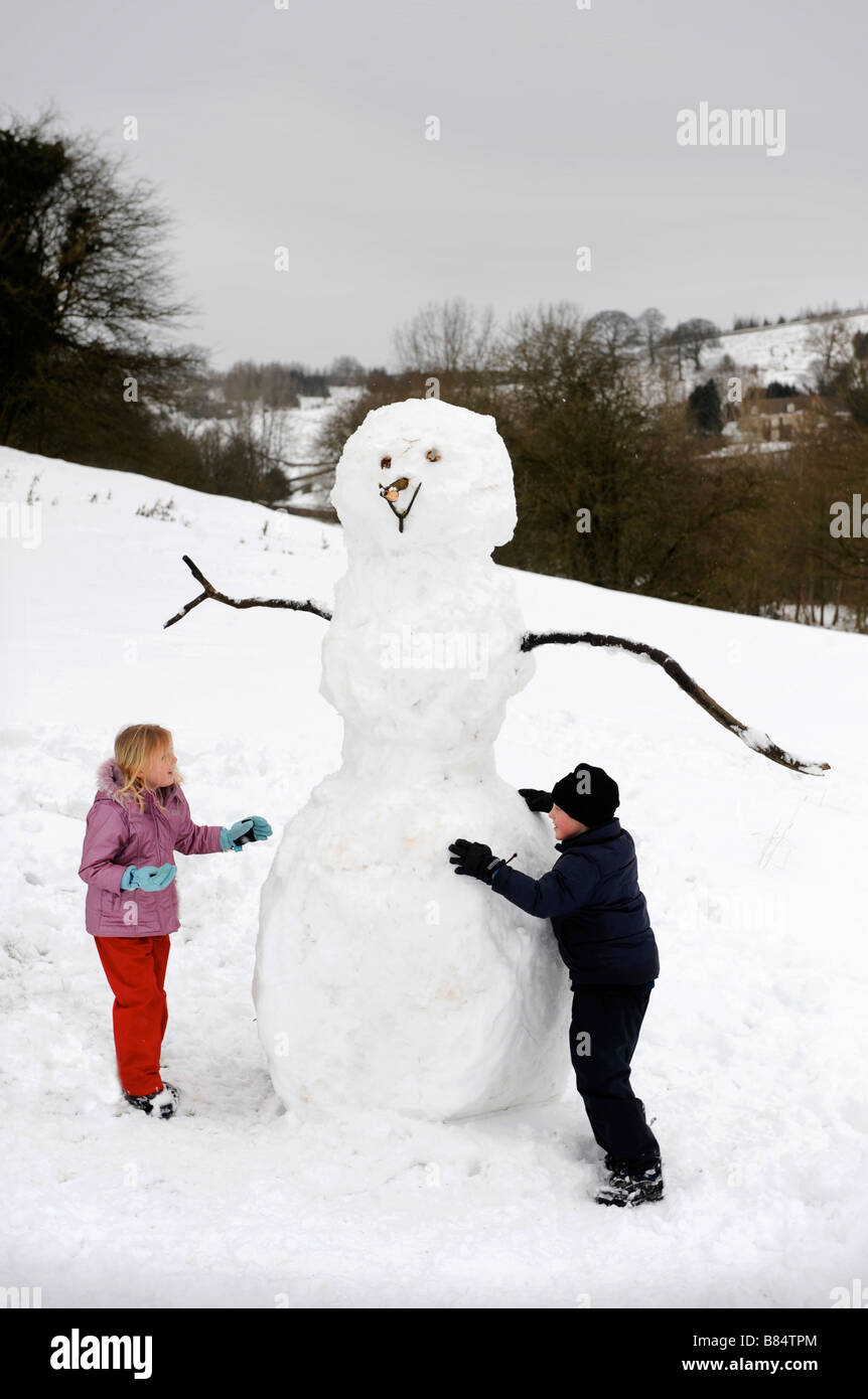 A YOUNG GIRL AND BOY BUILDING A SNOWMAN IN THE COTSWOLD HILLS GLOUCESTERSHIRE UK Stock Photo