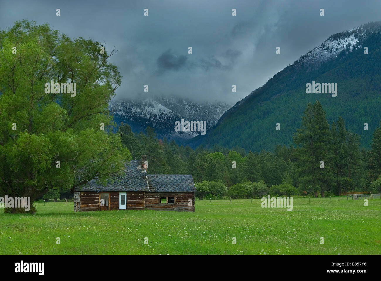 Old wooden house in a lush green field with mountains and a dramatic ...