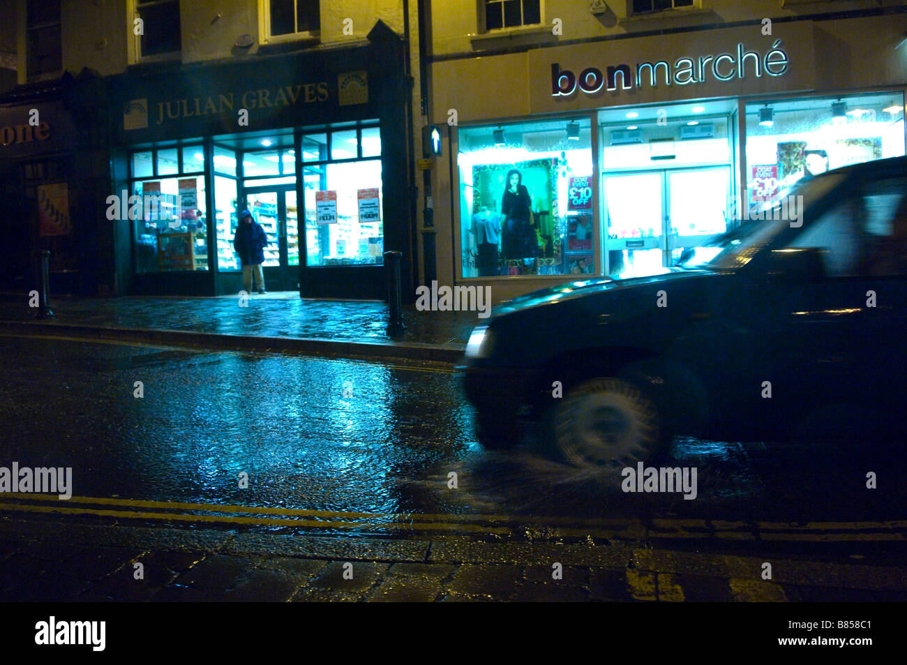A car drives through a puddle of water on a wet and windy night at