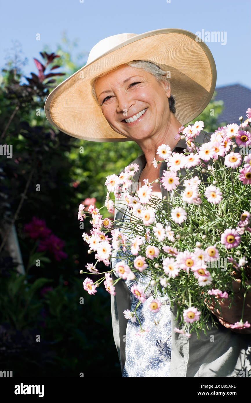 portrait of mature woman in gardening outfit holding flowers Stock ...