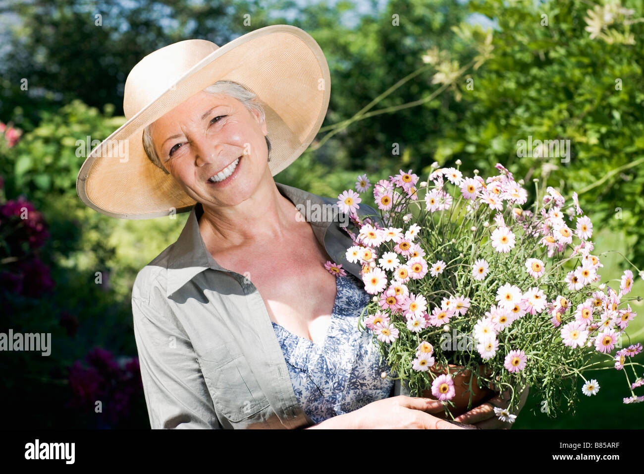 portrait of mature woman in gardening outfit holding flowers Stock ...