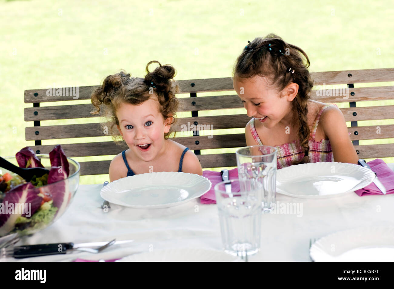 two little sisters sitting at table in garden having fun Stock Photo ...