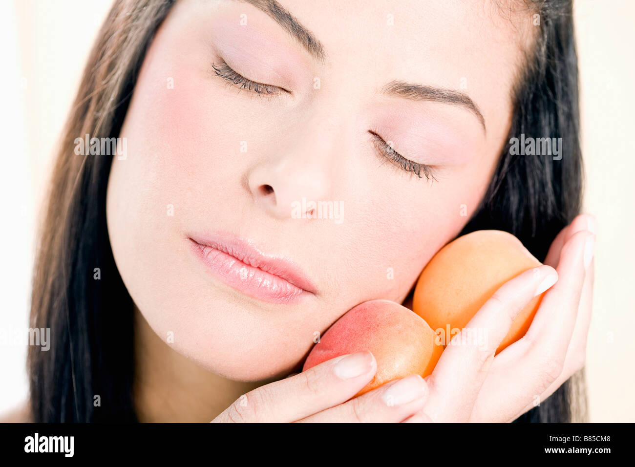 headshot of young woman holding peaches against her cheek Stock Photo
