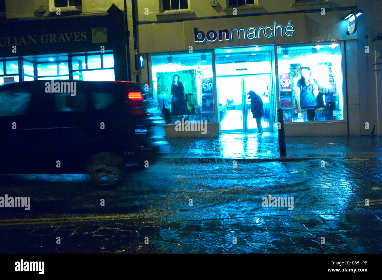 A car drives through a puddle of water on a wet and windy night at