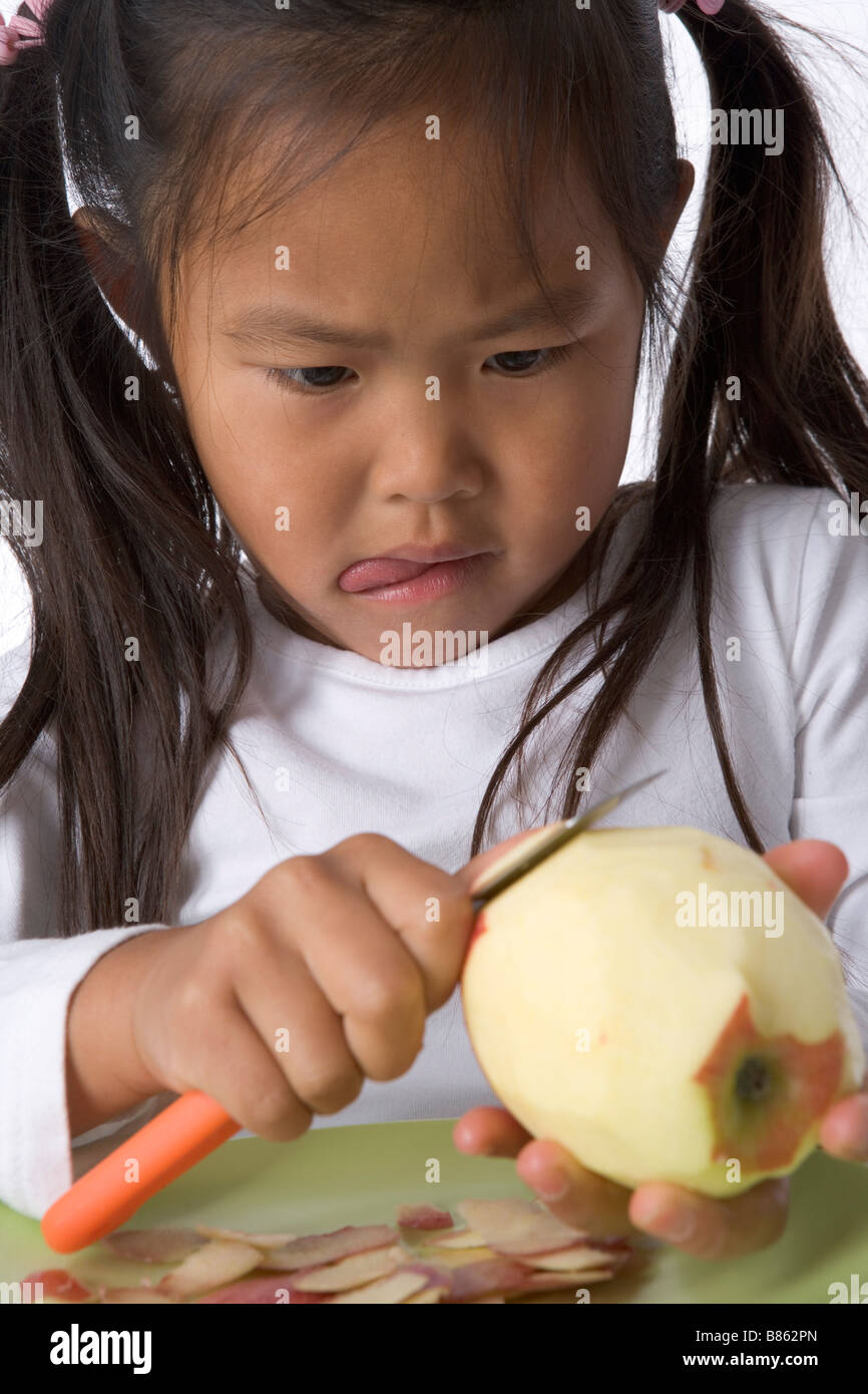 Little girl is peels an apple with a knife Stock Photo