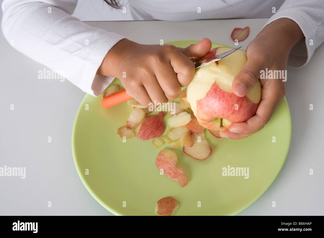 Little girl is peels an apple with a knife Stock Photo