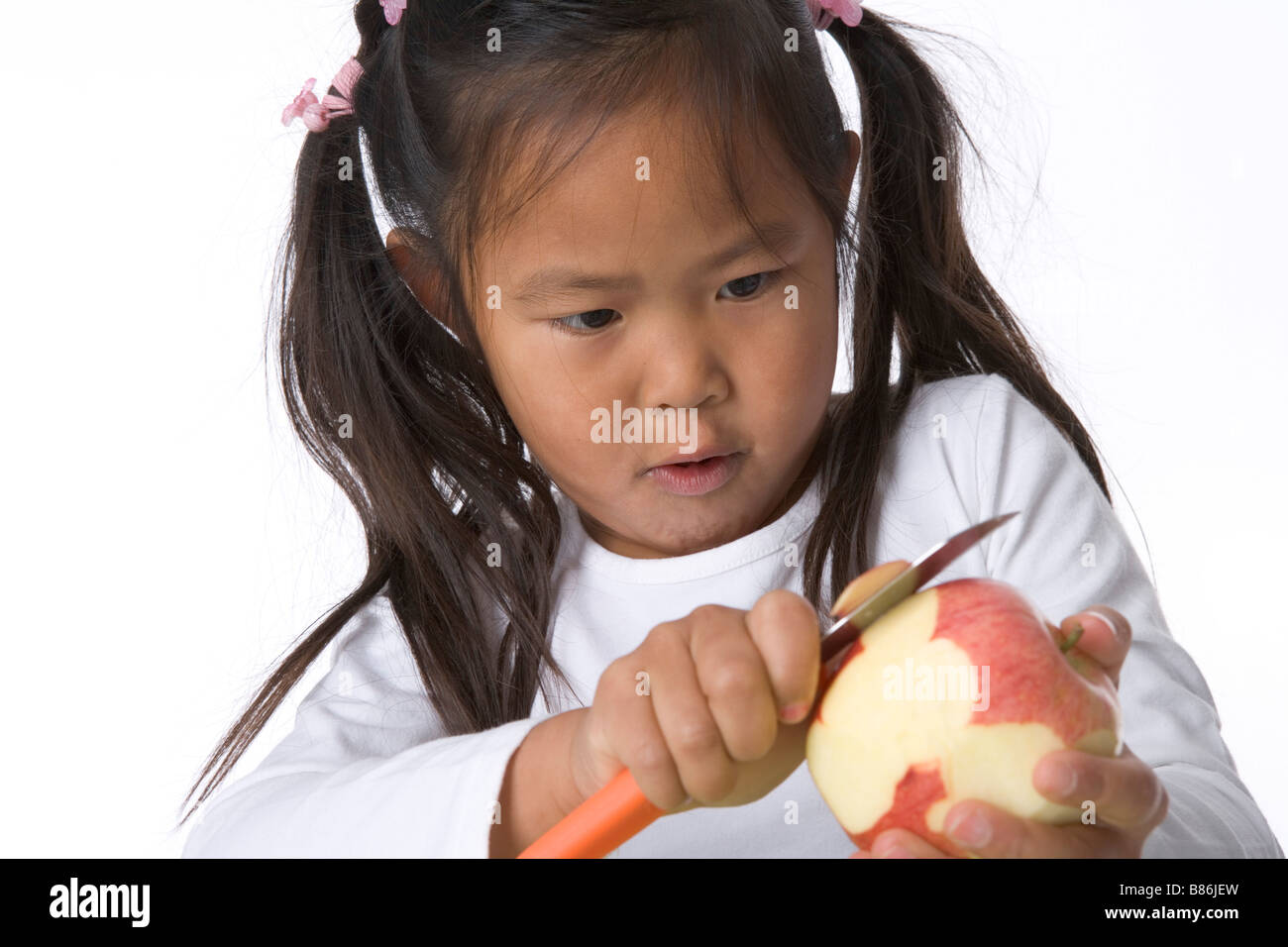 Little girl is peels an apple with a knife Stock Photo